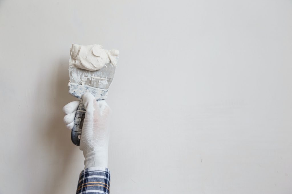 Worker in white gloves performs plastering of the walls of the room